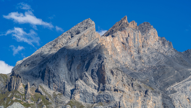 View of the sharp jagged mountain peaks with grey rock faces under a clear blue sky with light clouds in Kandersteg Canton of Bern Switzerland. View of the sharp jagged mountain peaks with grey rock faces under a clear blue sky with light clouds in Kandersteg Canton of Bern Switzerland.