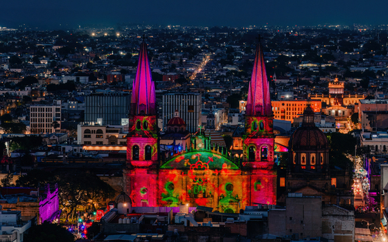 Aerial view of Guadalajara Cathedral illuminated with vibrant light projections at night set against the urban skyline of Guadalajara Jalisco Mexico.