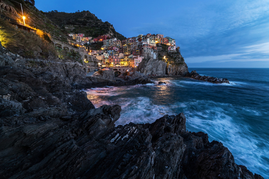View of the colorful village of Manarola perched on a cliff above the crashing waves of the Mediterranean Sea at twilight Manarola Liguria Italy. View of the colorful village of Manarola perched on a cliff above the crashing waves of the Mediterranean Sea at twilight Manarola Liguria Italy.
