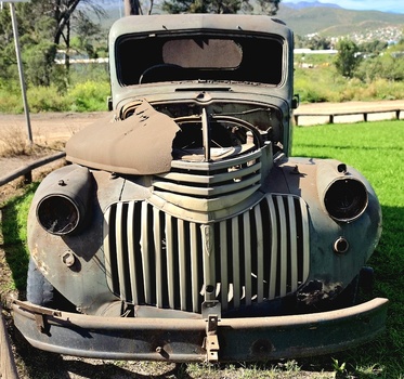 View of an abandoned vintage truck with a rusted grille and weathered body resting on green farmland in Ladismith Western Cape South Africa.