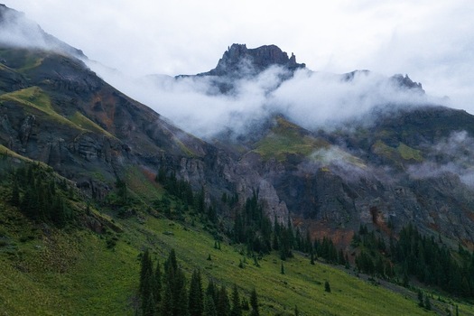 Aerial view of Mt. Sneffels in Yankee Boy Basin with rocky peaks green slopes pine trees and low hanging clouds in Ouray Colorado United States.