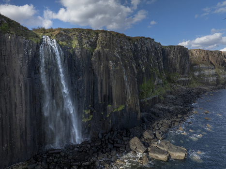 Aerial view of Mealt Falls cascading down dramatic basalt cliffs into the sea with rocky shoreline and blue sky in Scotland United Kingdom. Aerial view of Mealt Falls cascading down dramatic basalt cliffs into the sea with rocky shoreline and blue sky in Scotland United Kingdom.