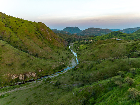 Aerial view of a winding river flowing through lush green hills and valleys in the Aravalli range near Udaipur Rajasthan India.
