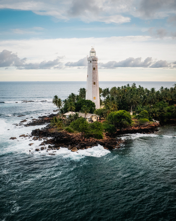 Aerial view of Dondra Lighthouse surrounded by lush palm trees and rocky coastline with crashing waves under a cloudy sky in Dondra Southern Province Sri Lanka. Aerial view of Dondra Lighthouse surrounded by lush palm trees and rocky coastline with crashing waves under a cloudy sky in Dondra Southern Province Sri Lanka.