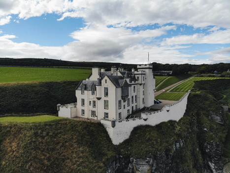 Aerial view of Dunbeath Castle perched on a cliffside with manicured lawns and green fields in the background in Dunbeath Scotland United Kingdom. Aerial view of Dunbeath Castle perched on a cliffside with manicured lawns and green fields in the background in Dunbeath Scotland United Kingdom.