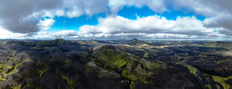 Aerial view of stark dark volcanic highlands contrasted by vivid green moss and winding glacial rivers under a dynamic sky Skaftárhreppur Iceland. Aerial view of stark dark volcanic highlands contrasted by vivid green moss and winding glacial rivers under a dynamic sky Skaftárhreppur Iceland.