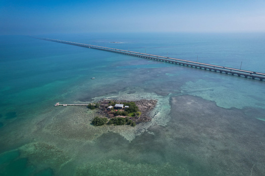 Aerial view of The Overseas Highway stretching across turquoise waters near a small private island with a dock and building in Key Largo Florida United States. Aerial view of The Overseas Highway stretching across turquoise waters near a small private island with a dock and building in Key Largo Florida United States.