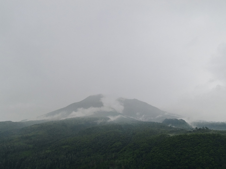 Aerial view of a mountain peak shrouded in mist and low clouds above dense green forests in Tawangmangu Central Java Indonesia.