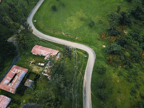Aerial view of a winding asphalt road snaking through vibrant green hills past rustic buildings with weathered red roofs Obudu Cross River Nigeria.