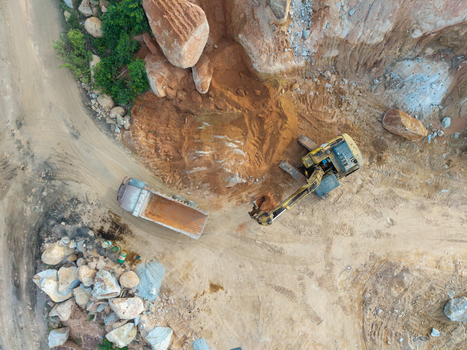 Aerial view of an excavator loading a dump truck at a mining site with piles of earth and rocky terrain in Bukit Tambun Penang Malaysia. Aerial view of an excavator loading a dump truck at a mining site with piles of earth and rocky terrain in Bukit Tambun Penang Malaysia.
