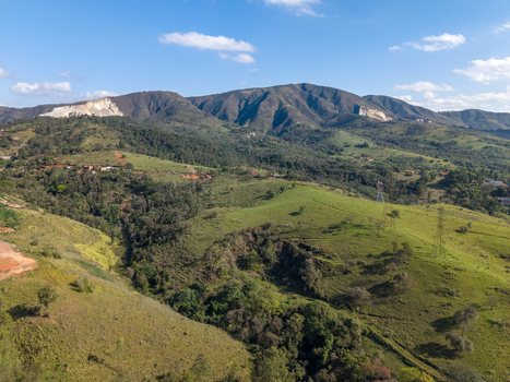 Aerial view of rolling green hills and mountains under a blue sky with scattered clouds in Brazil.