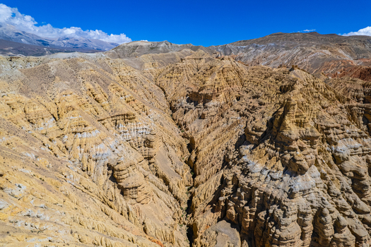 Aerial view of the rugged golden hued eroded rock formations and deep canyons of the Himalayan landscape under a clear blue sky in Nepal.
