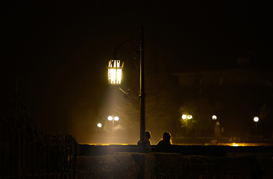 View of a couple standing near an ornate street lamp on a stone bridge at night in Ronda Andalusia Spain.