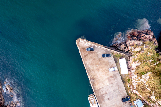 Aerial view of a concrete pier with parked cars and a small boat docked alongside the rocky coastline of Kincasslagh County Donegal Ireland. Aerial view of a concrete pier with parked cars and a small boat docked alongside the rocky coastline of Kincasslagh County Donegal Ireland.