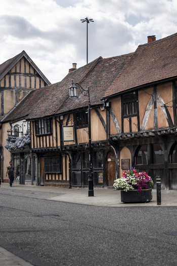 Coventry England United Kingdom 20 July 2026 View of the historic timber framed Ford s Hospital building with a flower planter on the sidewalk and a person walking along the street.