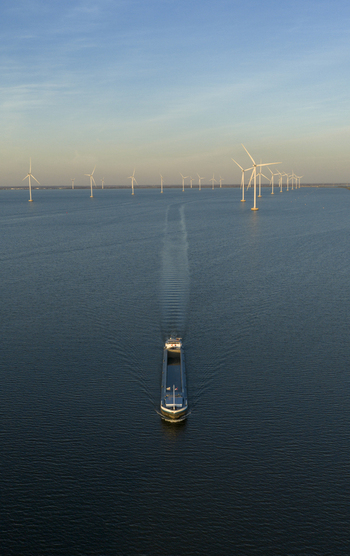 Aerial view of a cargo ship sailing through an offshore wind farm on calm blue water Netherlands. Aerial view of a cargo ship sailing through an offshore wind farm on calm blue water Netherlands.