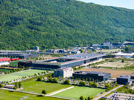 Aerial view of the Biel Bienne Boezingenfeld Champ industrial area featuring modern commercial buildings and sports fields near a lush forested mountain in Biel Bienne Canton of Bern Switzerland.