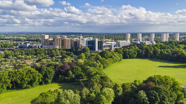 Aerial view of Gunnersbury Park with green lawns and mature trees featuring the urban skyline of London in the background under a blue sky London England United Kingdom. Aerial view of Gunnersbury Park with green lawns and mature trees featuring the urban skyline of London in the background under a blue sky London England United Kingdom.