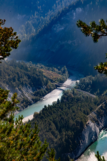 Aerial view of the Swiss Alps featuring a winding river and bridge in a deep valley surrounded by dense pine forests and steep rocky slopes in Airolo Ticino Switzerland. Aerial view of the Swiss Alps featuring a winding river and bridge in a deep valley surrounded by dense pine forests and steep rocky slopes in Airolo Ticino Switzerland.