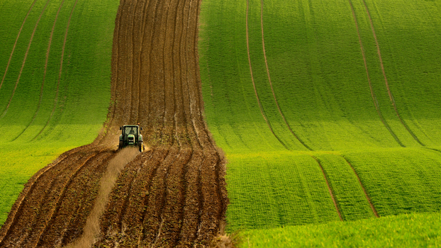 View of a tractor plowing a field in the rolling landscape of Moravia with deep furrows and vibrant green hills in Brno City District South Moravian Region Czechia.