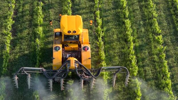 Aerial view of a tractor spraying a vineyard in France.