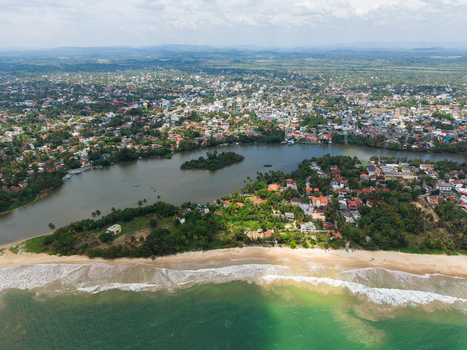 Aerial view of the Nilwala River flowing into the Indian Ocean sandy beach lush palm trees and urban landscape in Matara Southern Province Sri Lanka. Aerial view of the Nilwala River flowing into the Indian Ocean sandy beach lush palm trees and urban landscape in Matara Southern Province Sri Lanka.