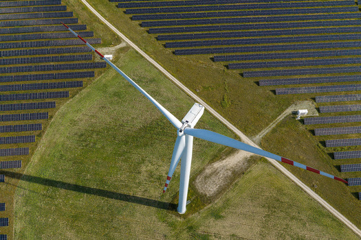 Aerial view of a wind turbine standing amidst rows of solar panels in a renewable energy farm in Poland.