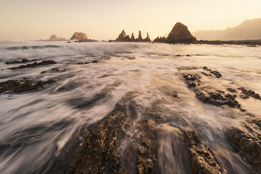 View of the sharp rock formations of Gueirua beach with crashing waves and long exposure water motion during sunset in Asturias Spain.
