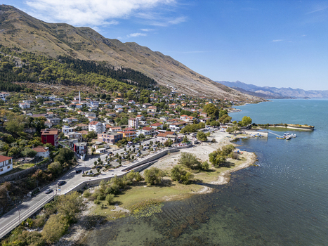 Aerial view of the village of Shiroka nestled between the mountains and the shores of Lake Shkodra with a coastal road and residential buildings in Shiroka Shkoder County Albania. Aerial view of the village of Shiroka nestled between the mountains and the shores of Lake Shkodra with a coastal road and residential buildings in Shiroka Shkoder County Albania.