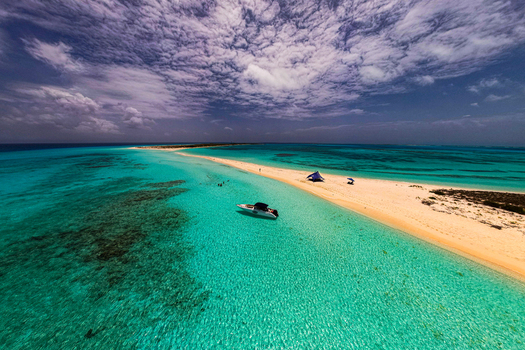 Aerial view of Los Roques archipelago featuring a white sandbar turquoise waters a motorboat anchored near the shore and a cloudy sky in Los Roques Dependencias Federales Venezuela. Aerial view of Los Roques archipelago featuring a white sandbar turquoise waters a motorboat anchored near the shore and a cloudy sky in Los Roques Dependencias Federales Venezuela.