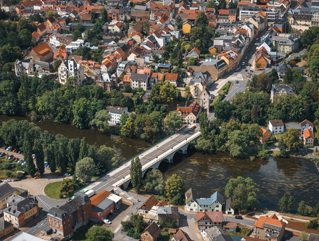 Aerial view of a stone bridge crossing the river in the historic town surrounded by dense trees and residential rooftops in Saalfeld Thuringia Germany. Aerial view of a stone bridge crossing the river in the historic town surrounded by dense trees and residential rooftops in Saalfeld Thuringia Germany.