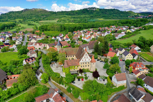 Wiesenthau Germany 02 May 2026 Aerial view of Schloss Wiesenthau surrounded by historic houses green trees and rolling hills under a blue sky with white clouds. Wiesenthau Germany 02 May 2026 Aerial view of Schloss Wiesenthau surrounded by historic houses green trees and rolling hills under a blue sky with white clouds.
