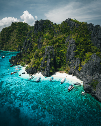 Aerial view of El Nido featuring limestone cliffs turquoise waters and traditional outrigger boats anchored at a white sand beach in El Nido Mimaropa Philippines. Aerial view of El Nido featuring limestone cliffs turquoise waters and traditional outrigger boats anchored at a white sand beach in El Nido Mimaropa Philippines.