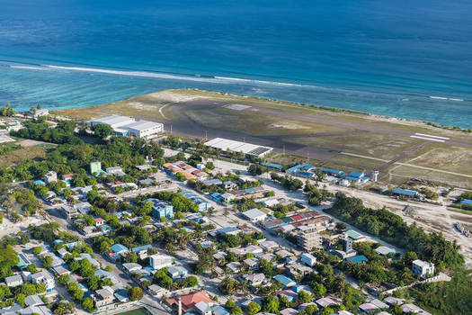 Aerial view of the airport runway and residential buildings surrounded by tropical trees and the Indian Ocean in Kudahuvadhoo Dhaalu Atoll Maldives.