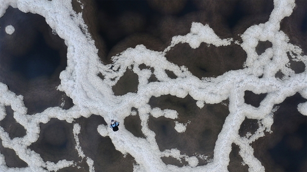 Aerial view of a lone figure traversing a mesmerizing labyrinth of brilliant white salt patterns against the deep dark waters Dead Sea Israel.