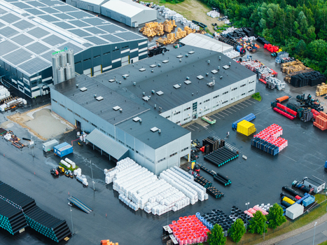 Jelgava Latvia 04 July 2026 Aerial view of a polymer pipe manufacturing facility with large industrial buildings stacks of pipes and storage areas on a wet asphalt surface.