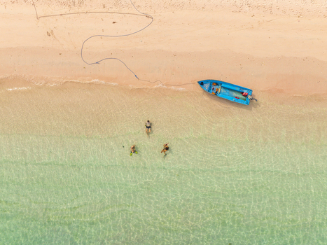 Aerial view of Pink Beach with a blue boat moored on the shore and people swimming in the clear turquoise water in East Nusa Tenggara Indonesia. Aerial view of Pink Beach with a blue boat moored on the shore and people swimming in the clear turquoise water in East Nusa Tenggara Indonesia.