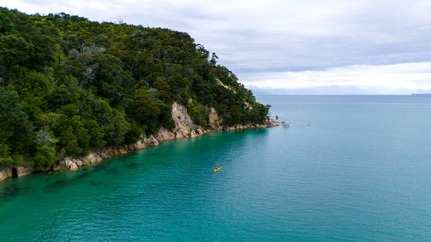 Aerial view of turquoise waters gently kissing the lush green coastline of Abel Tasman National Park a lone kayak drifting peacefully Abel Tasman National Park Tasman Region New Zealand. Aerial view of turquoise waters gently kissing the lush green coastline of Abel Tasman National Park a lone kayak drifting peacefully Abel Tasman National Park Tasman Region New Zealand.