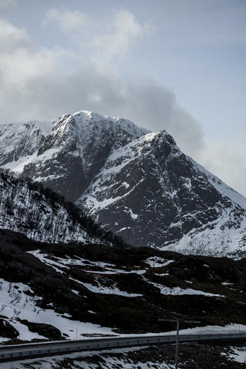View of snow covered mountain peaks under a dramatic cloudy sky with a winding road in the foreground Kvaloya Troms Norway. View of snow covered mountain peaks under a dramatic cloudy sky with a winding road in the foreground Kvaloya Troms Norway.