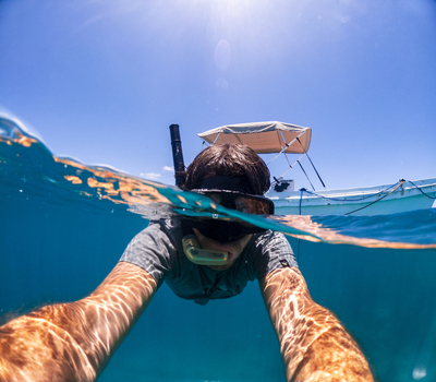 View of a man snorkeling in crystal clear turquoise water with a boat in the background under a bright sun in Guanaja Bay Islands Department Honduras. View of a man snorkeling in crystal clear turquoise water with a boat in the background under a bright sun in Guanaja Bay Islands Department Honduras.