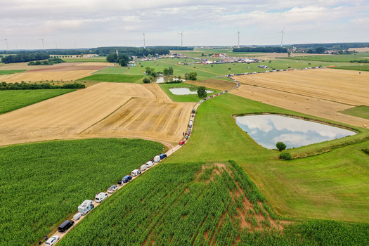 Aerial view of a long line of vehicles on a rural road leading to the Open Beatz Festival across agricultural fields with ponds and wind turbines Herzogenaurach Bayern Germany. Aerial view of a long line of vehicles on a rural road leading to the Open Beatz Festival across agricultural fields with ponds and wind turbines Herzogenaurach Bayern Germany.