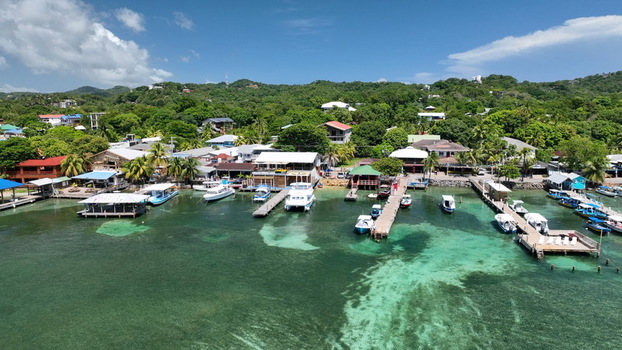 Aerial view of West End with boats docked at wooden piers along the turquoise coastline surrounded by lush hills and tropical vegetation in West End Bay Islands Department Honduras. Aerial view of West End with boats docked at wooden piers along the turquoise coastline surrounded by lush hills and tropical vegetation in West End Bay Islands Department Honduras.