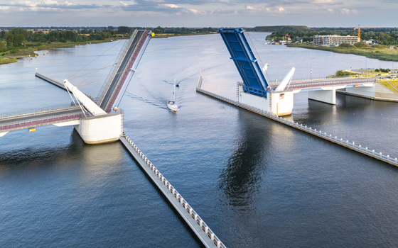 Aerial view of the Sobieszewo drawbridge with a boat passing through the open span surrounded by calm water and green banks in Gdansk Pomeranian Voivodeship Poland.