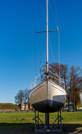 View of a sailboat on a metal stand in a park with trees and buildings in the background in Klaipeda Klaipeda County Lithuania. View of a sailboat on a metal stand in a park with trees and buildings in the background in Klaipeda Klaipeda County Lithuania.