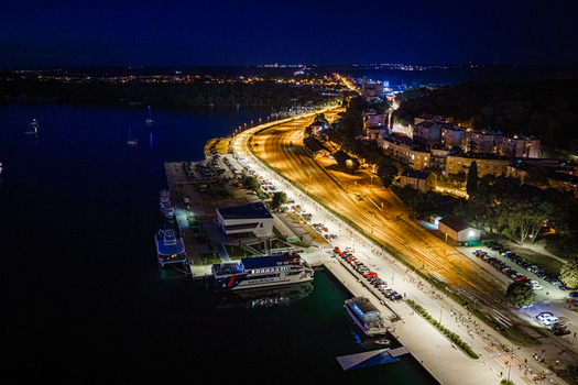 Aerial view of the illuminated waterfront and harbor at night featuring docked boats coastal roads and city lights reflecting on the water in Pula Istria County Croatia. Aerial view of the illuminated waterfront and harbor at night featuring docked boats coastal roads and city lights reflecting on the water in Pula Istria County Croatia.