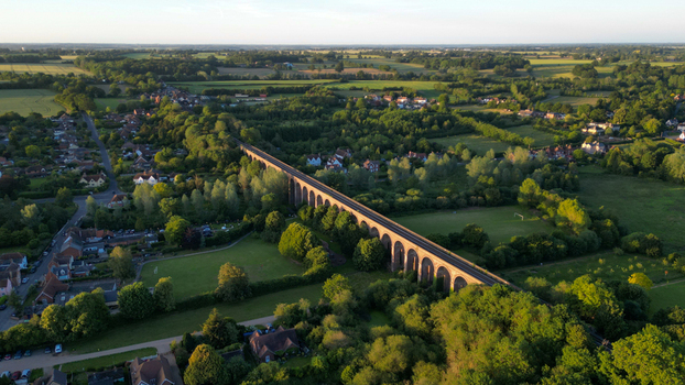 Aerial view of Chappel Viaduct a historic brick railway bridge spanning the lush green landscape of the English countryside with surrounding trees in Chappel England United Kingdom.