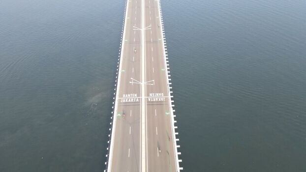 Aerial view of the Pantai Indah Kapuk 2 bridge spanning over the water with road markings indicating Jakarta and Banten in Kecamatan Penjaringan Banten Indonesia. Aerial view of the Pantai Indah Kapuk 2 bridge spanning over the water with road markings indicating Jakarta and Banten in Kecamatan Penjaringan Banten Indonesia.