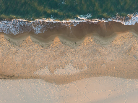 Aerial view of the sandy coastline of the Baltic Sea with gentle waves washing onto the shore and footprints visible in the sand in Gdansk Pomeranian Voivodeship Poland.