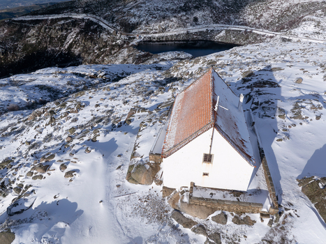 Aerial view of a solitary white building with a red roof amidst a snow covered landscape near a dark tranquil lake Lagoa Comprida São Romão Serra da Estrella Portugal. Aerial view of a solitary white building with a red roof amidst a snow covered landscape near a dark tranquil lake Lagoa Comprida São Romão Serra da Estrella Portugal.