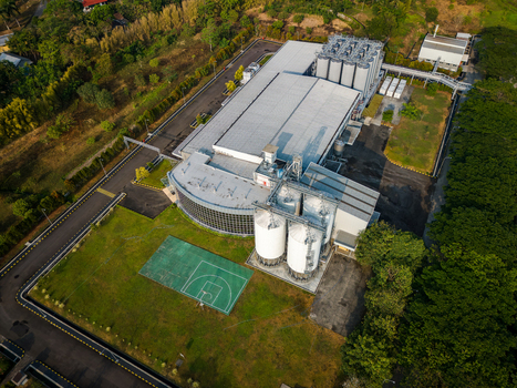 Aerial view of an industrial facility with large storage silos a factory building and an adjacent basketball court surrounded by trees in Semarang Regency Central Java Indonesia. Aerial view of an industrial facility with large storage silos a factory building and an adjacent basketball court surrounded by trees in Semarang Regency Central Java Indonesia.